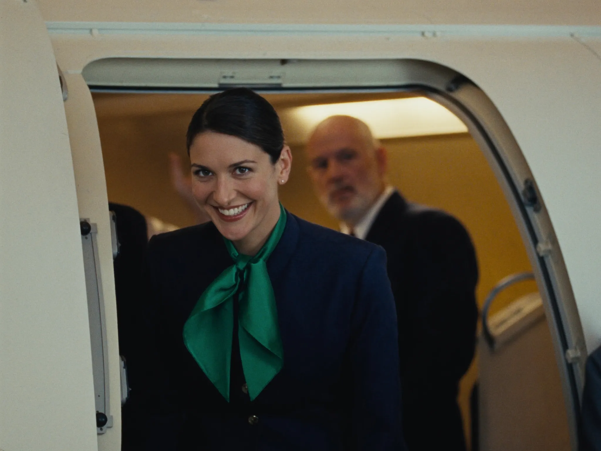 Comissária sorrindo na porta do avião recebendo os passageiros no embarque
