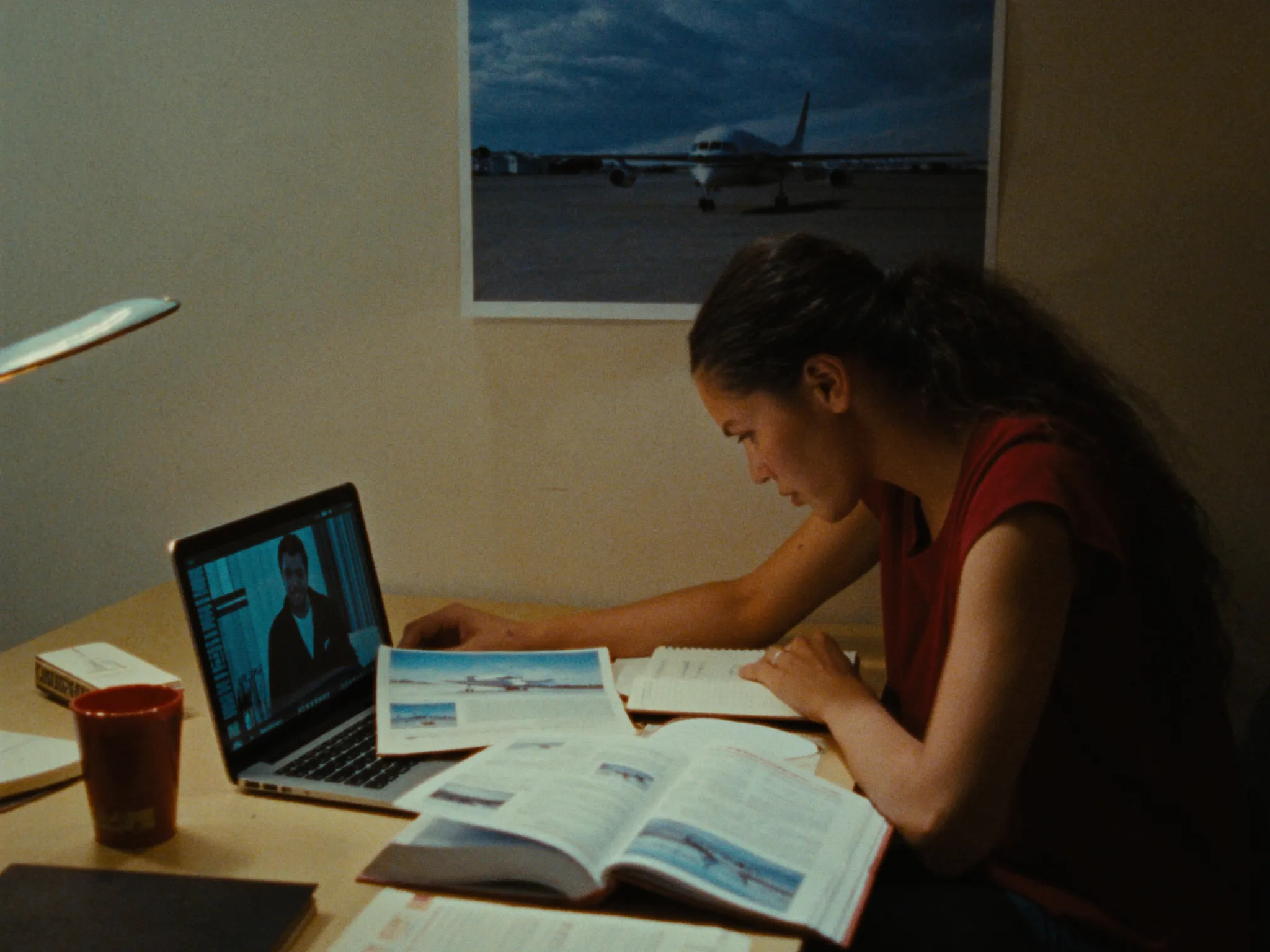 Jovem estudando à noite na mesa de casa com livro de aviação e a foto de um avião na parede